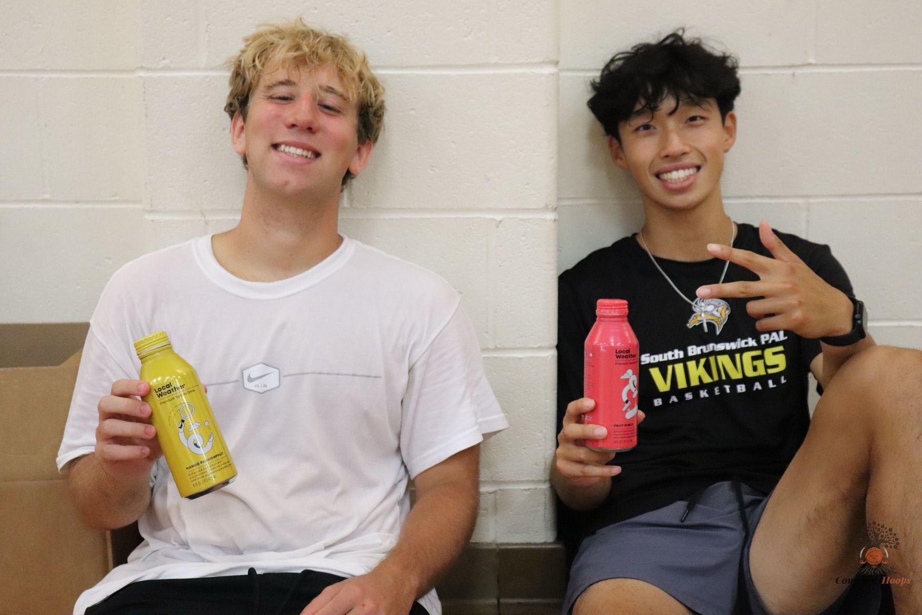 Two players sitting against the gym wall with sports drinks